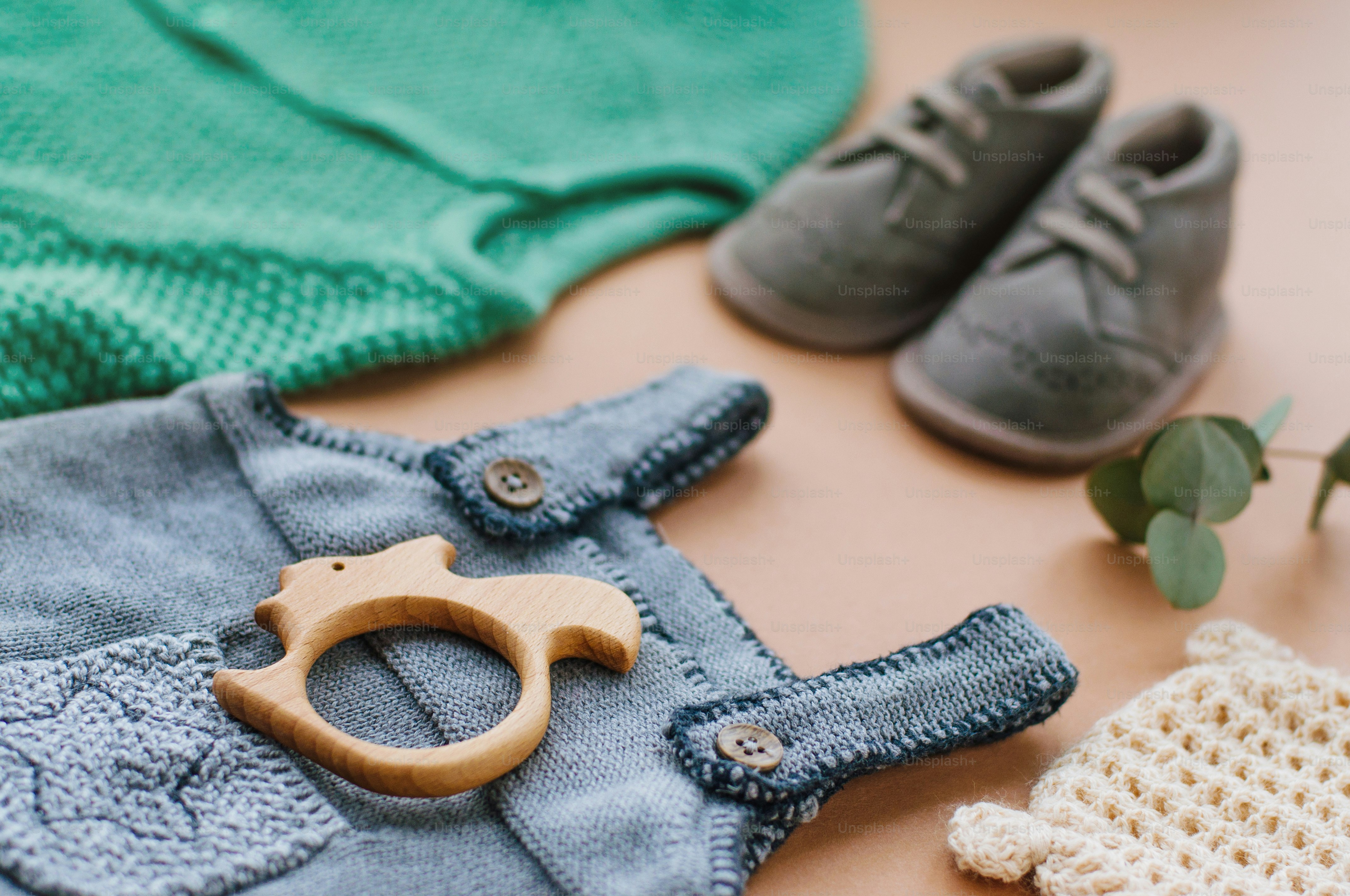 Baby clothes concept. Close up of baby knitted clothes and shoes on beige background near wooden teether squirrel.