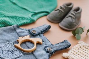 Baby clothes concept. Close up of baby knitted clothes and shoes on beige background near wooden teether squirrel.