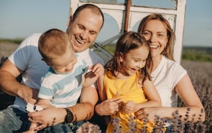 Belle famille souriante tout en tenant leurs enfants dans un champ de lavande pendant une journée d’été ensoleillée