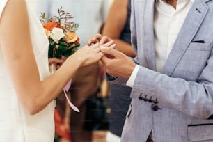 Braut mit Blumenstrauß und Bräutigam tauschen Eheringe am Hochzeitsstand. Stilvolles Paar Offizielle Hochzeitszeremonie