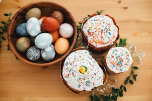 Homemade easter cake and stylish easter eggs natural dyed in wooden bowl on rustic table with flowers. Happy Easter. Traditional Easter bread. Flat lay