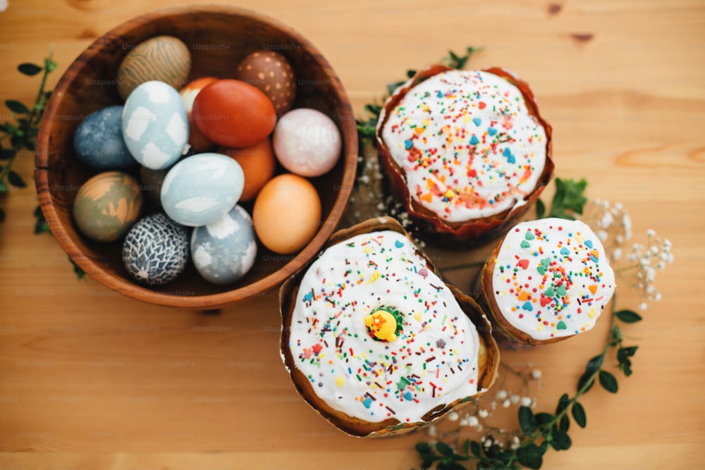 Gâteau de Pâques fait maison et oeufs de Pâques élégants teints au naturel dans un bol en bois sur une table rustique avec des fleurs. Joyeuses Pâques. Pain traditionnel de Pâques. Pose à plat