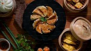 Vue de dessus de Dim sum avec des boulettes de gyoza japonais frites sur une assiette noire, des boulettes chinoises et des petits pains servis sur un cuiseur vapeur traditionnel