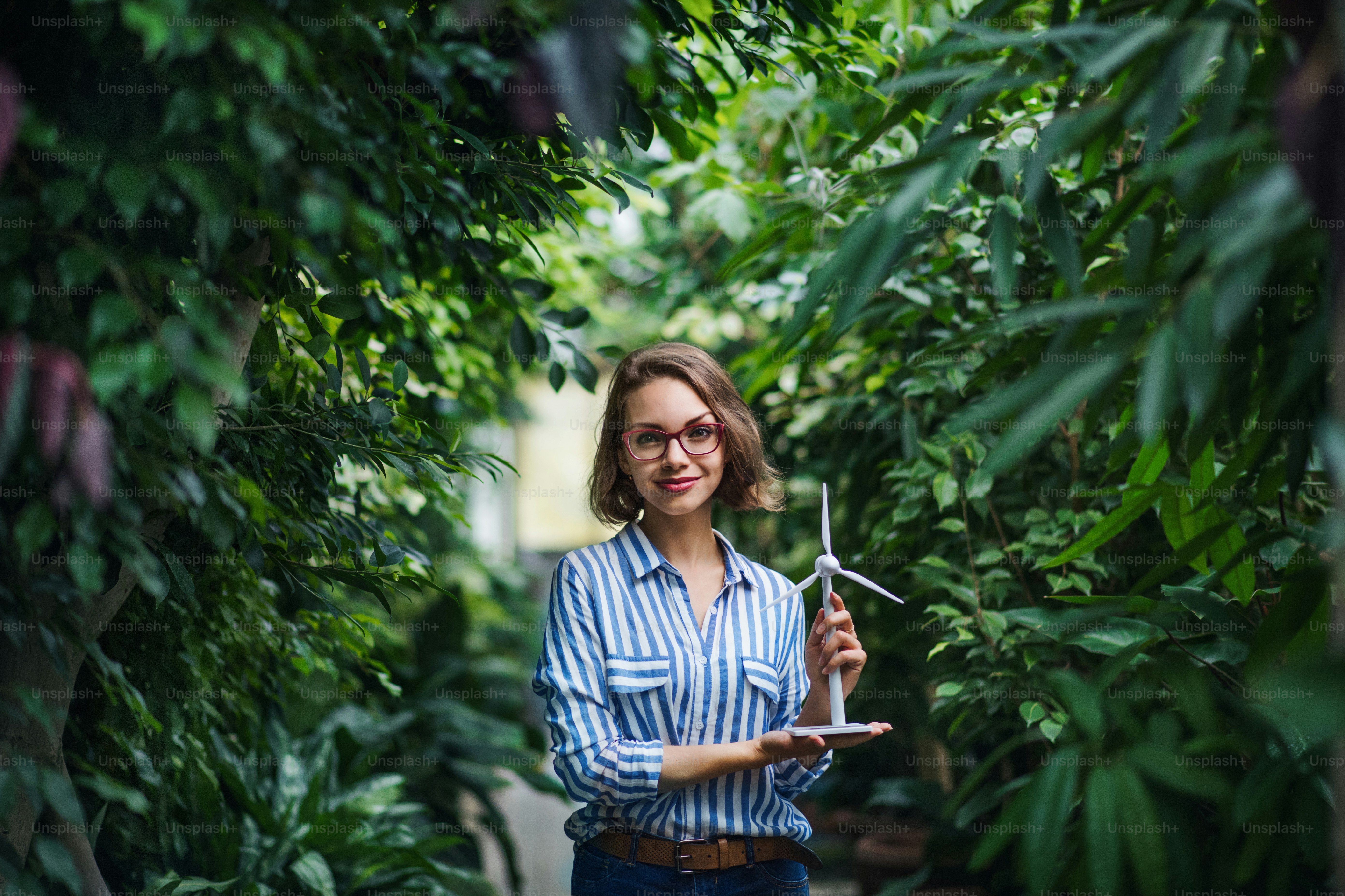 Young woman with windmill model standing in botanical garden. Copy space