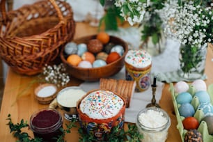 イースターモダンエッグ、イースターパン、ハム、ビート、バター、緑の枝、花が籐のバスケットとキャンドル付きの素朴な木製のテーブルの上。教会での祝福のための伝統的なイースターフード