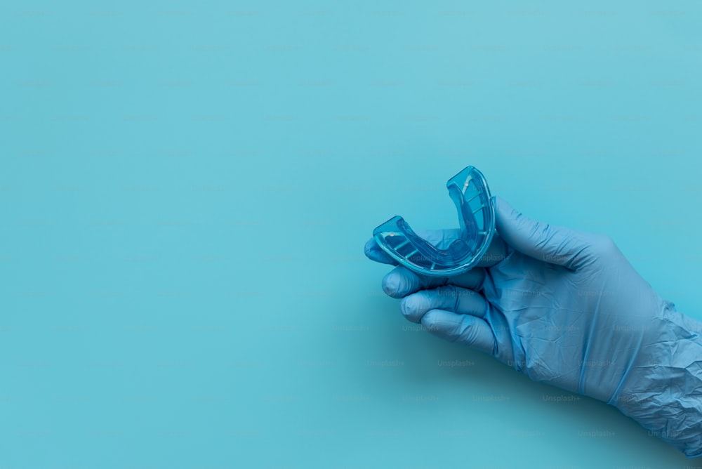 Hand of medic wearing blue latex glove holding myofunctional trainer on blue background. Teeth correction concept
