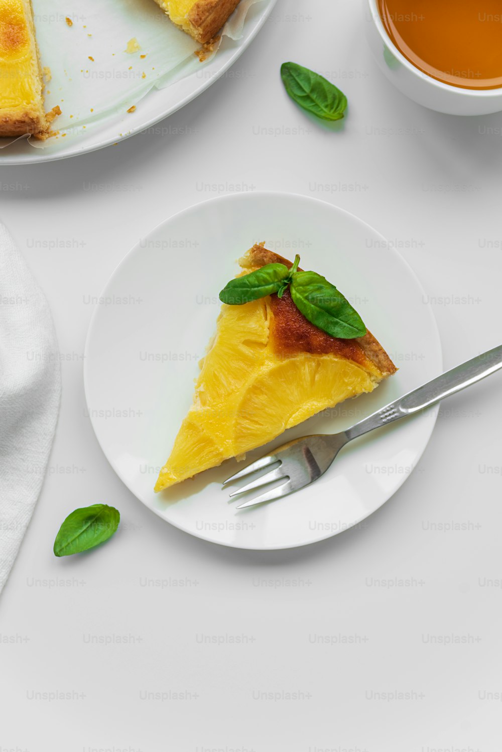 Gâteau à l’ananas renversé tranché décoré de feuilles vertes avec une tasse de thé sur une table blanche. Dessert tropical d’été. Vue de dessus. Espace de copie