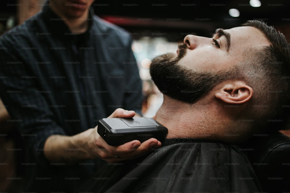 Good looking young adult man getting a hair and beard styling and dressing treatment by professional hairstylist.