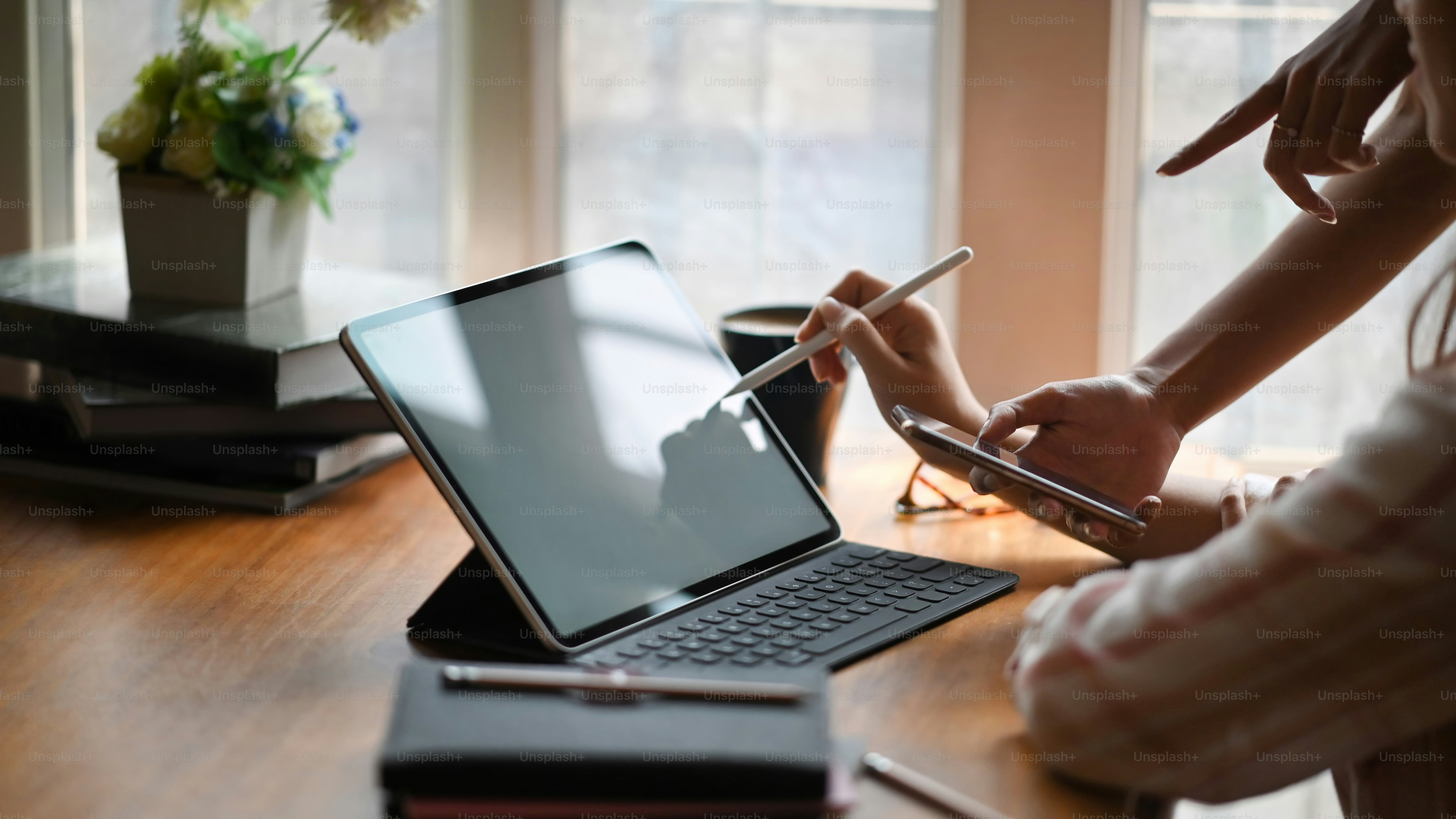 Side image of beautiful woman in striped shirt drawing on white blank screen computer tablet according information by her friends that standing next to her with orderly living room as background.