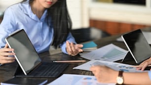 비즈니스 개발 팀이 컴퓨터 노트북, 태블릿 및 문서 정보를 가지고 현대적인 회의 테이블에서 토론/대화/회의하는 잘린 이미지.