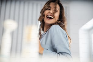 Mujer linda feliz sosteniendo rizador mientras baila en el dormitorio foto almacenada