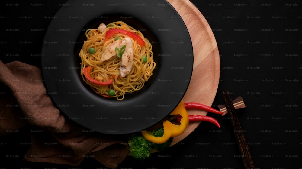 Top view of Schezwan Noodles or Chow Mein with vegetable, chicken and chilli sauce served in black plate