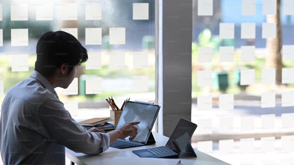 Foto de hombre de negocios usando/escribiendo en una tableta de computadora con funda de teclado mientras está sentado en la mesa de trabajo moderna con un lugar de trabajo ordenado como fondo.