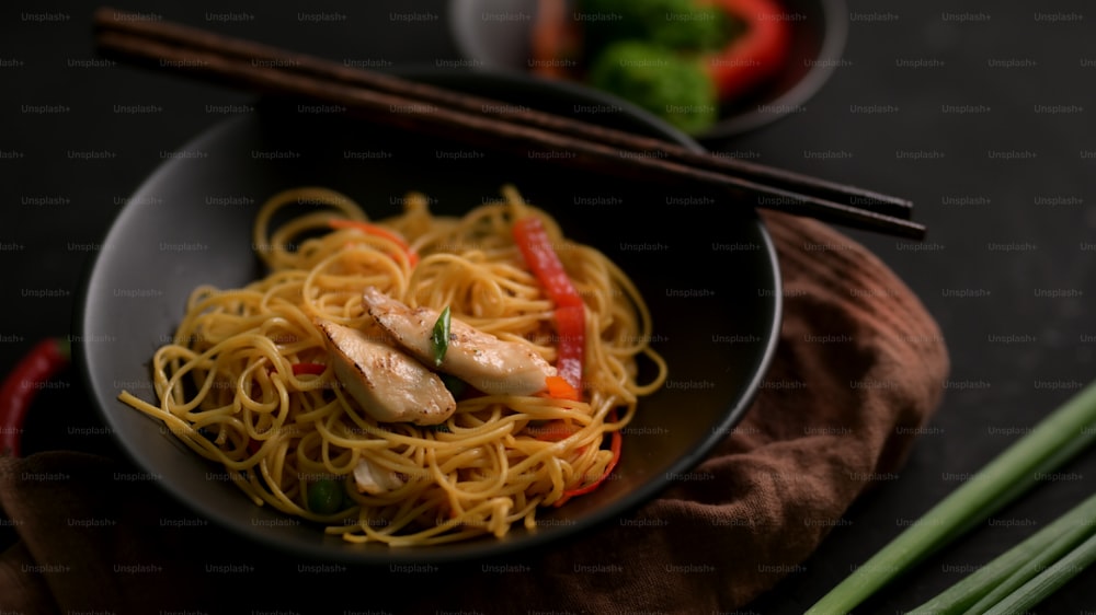 Close up view of Schezwan Noodles or Chow Mein in black bowl with chopsticks  on black table
