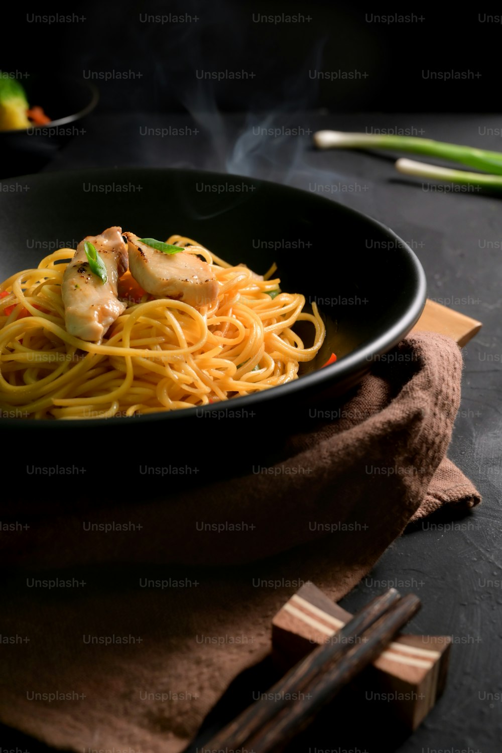 Abgeschnittene Aufnahme von Schezwan Nudeln oder Chow Mein in schwarzer Schüssel auf schwarzem Tisch mit Stäbchen