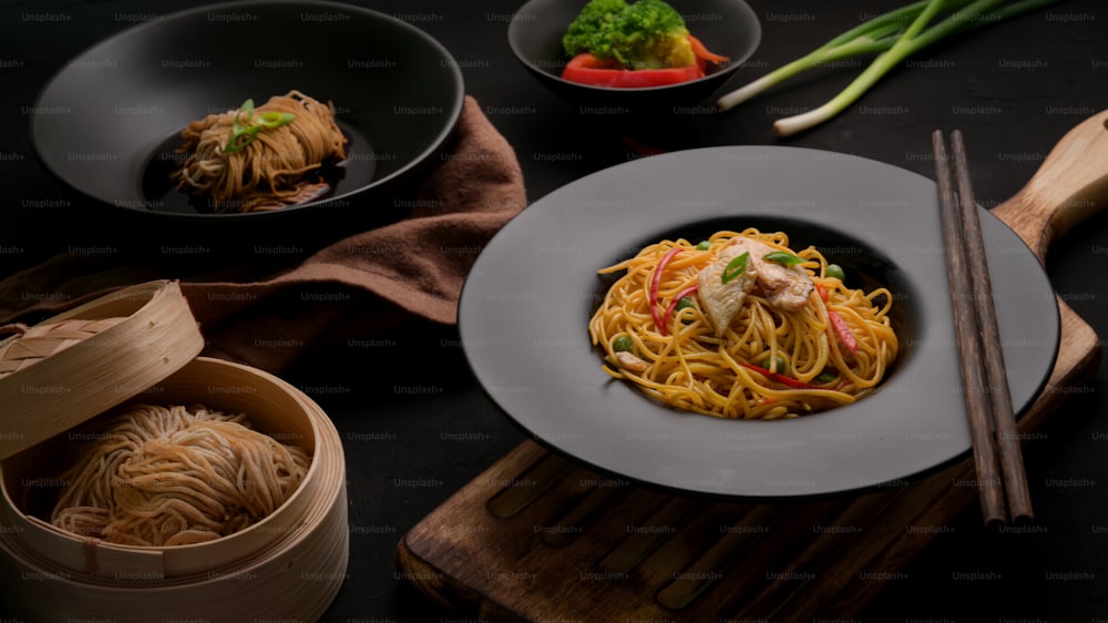 Shot recadré de nouilles Schezwan ou de Chow Mein avec des légumes, du poulet et de la sauce pimentée servis dans une assiette noire sur une table noire dans un restaurant chinois