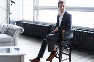 Portrait of confidence. Thoughtful young man in full suit looking away while sitting on the stool