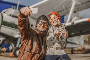 비행사 안경을 쓰고 스마트폰을 사용하고 아이와 함께 사진을 찍는 행복한 남성 스톡 사진