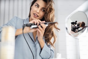 Smiling young lady doing hairstyle in front of the mirror in the room stock photo
