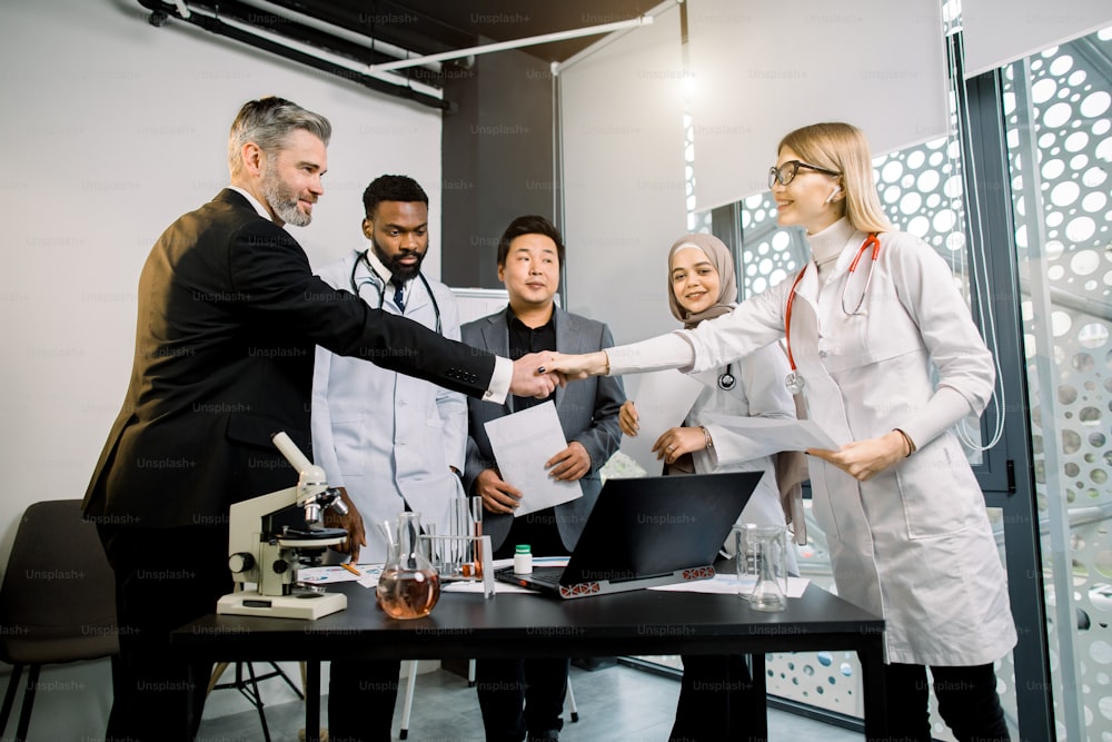 Team of doctors, scientists, pharmaceutical workers having meeting in modern lab with equipment. Caucasian man and woman shaking hands, after successful cooperation and results.