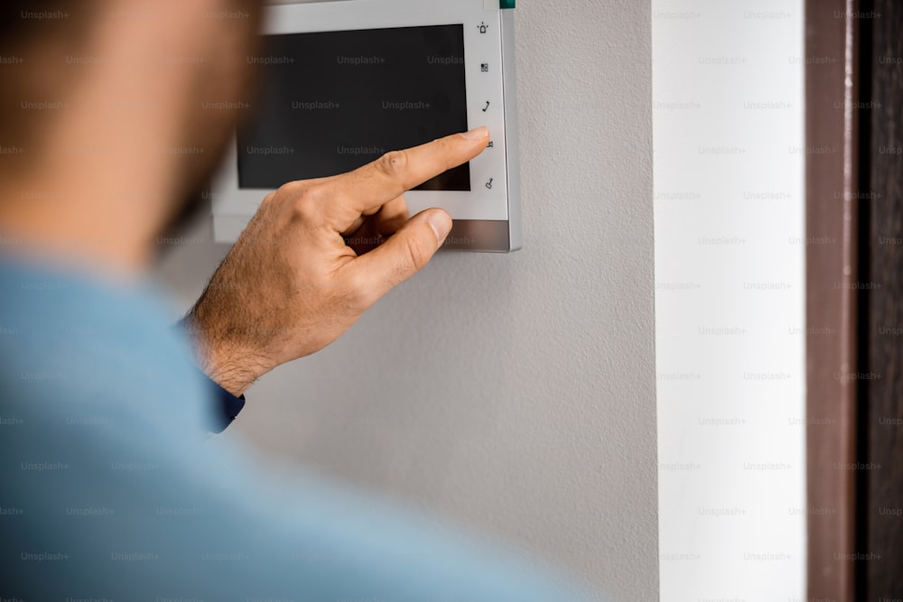 Primo piano della mano maschile che preme il pulsante per sbloccare il videocitofono sul muro di casa. Banner del sito web