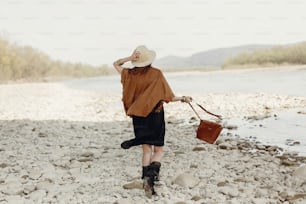 happy stylish hipster traveler woman in hat, fringe poncho back view, walking near  river, gypsy boho girl. wanderlust summer travel. atmospheric moment. space for text.