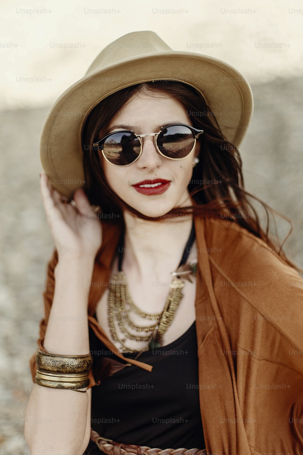 Schönes stilvolles Hipster-Frauenporträt in Sonnenbrille mit Hut, mit windigen Haaren. Boho Reisendes Mädchen im Zigeunerlook, in Strandnähe in den Bergen. atmosphärischer Moment. Sommerreisen.