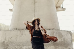 stylish hipster woman having fun and smiling, in hat with windy hair near river stones. boho traveler girl in gypsy look. summer travel. atmospheric moment. space for text.