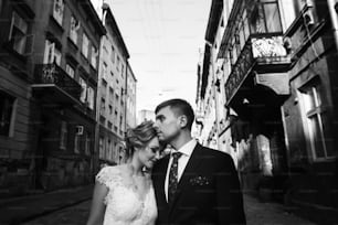 Romantic, sensual couple of newlyweds posing outdoors in old european street, family portrait of handsome groom hugging smiling bride