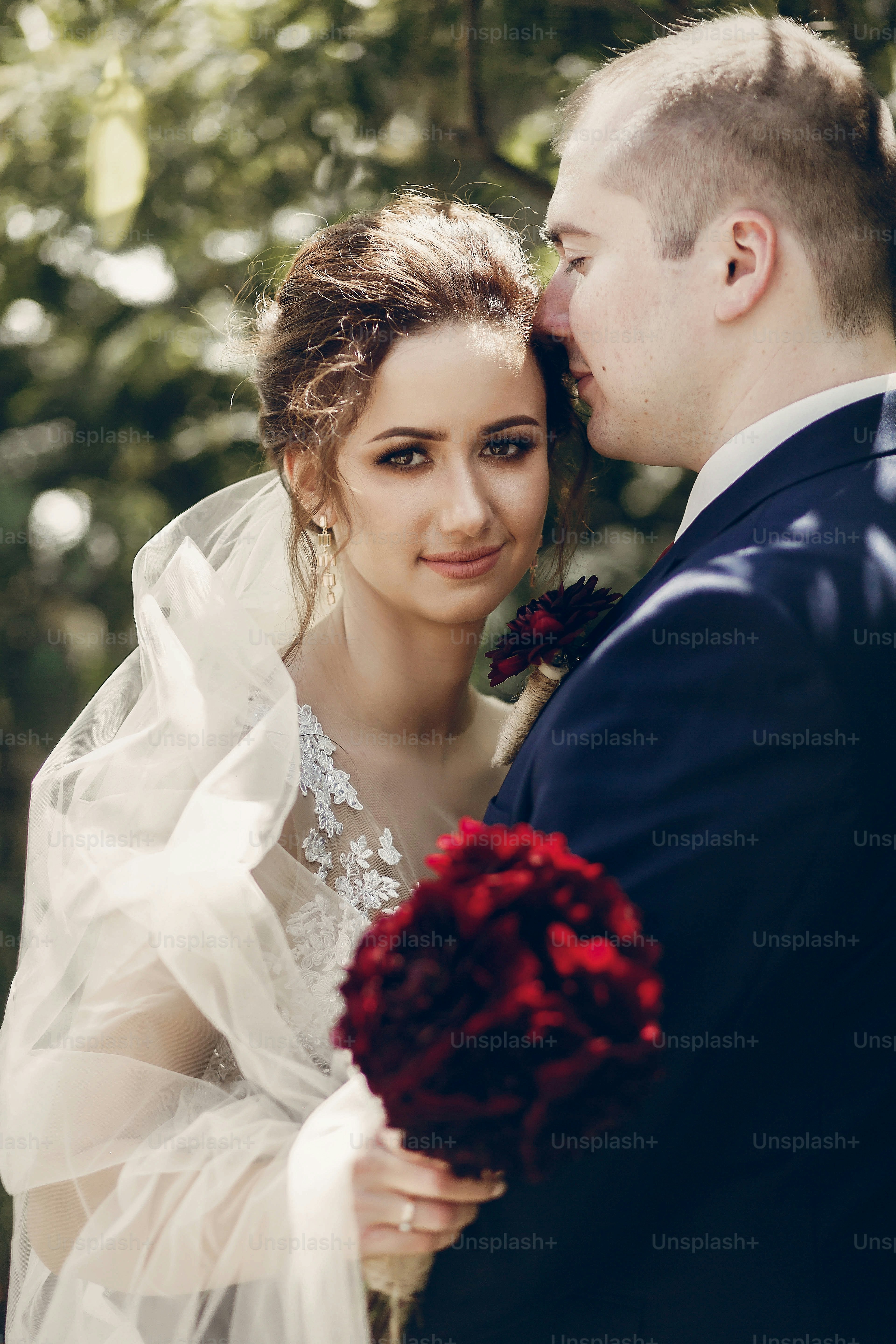 Happy newlywed couple hugging outdoors, portrait of groom kissing bride in white wedding dress in a summer park, happy moment concept