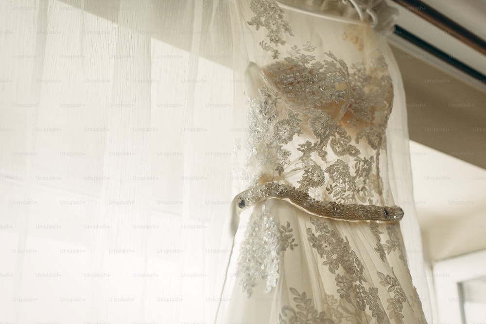 호텔 방의 창문 근처에 매달려 있는 아름다운 흰색 웨딩 드레스, 아침 결혼식 준비, 옷걸이 클로즈업에 신부를 위한 흰색 레이스 드레스