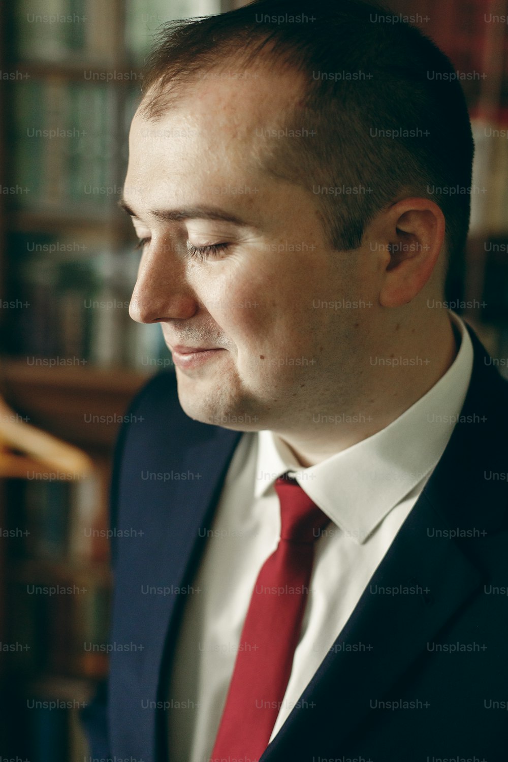Happy stylish groom in dark blue suit with red tie posing in hotel room morning before the wedding, portrait of a happy businessman indoors