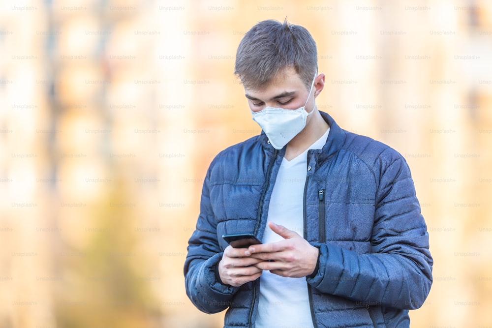 Young man with protective mask on his face communicates from mobile phone. Coronavirus Covid-19 concept.