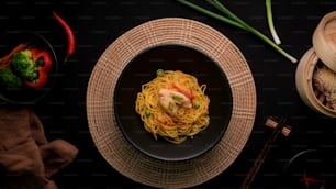 Draufsicht auf Schezwan Nudeln oder Chow Mein mit Gemüse, Hühnchen und Chilisauce serviert in schwarzer Schüssel und Zutaten auf schwarzem Tisch