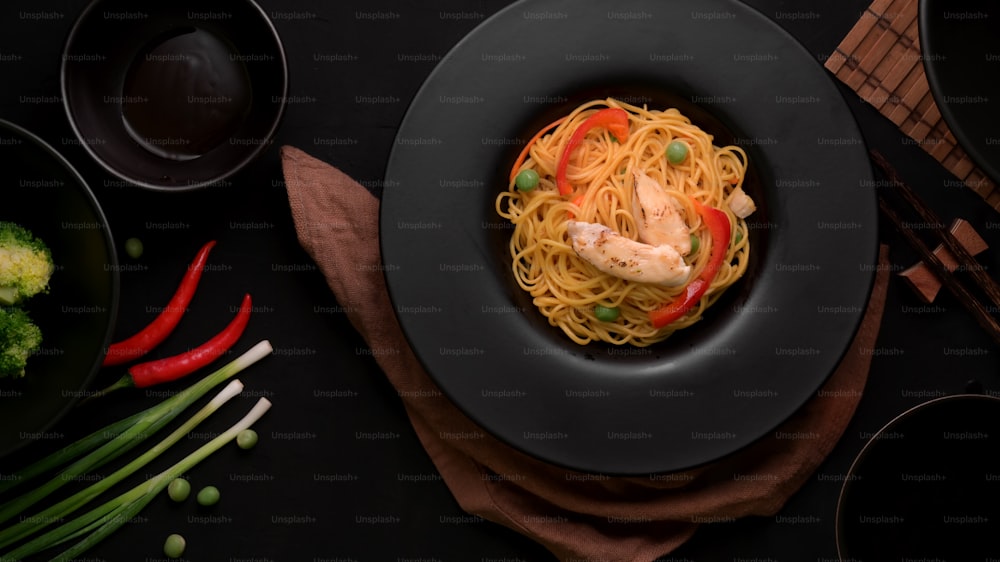 Draufsicht auf Schezwan Nudeln oder Chow Mein mit Gemüse und Hühnchen serviert in schwarzem Teller auf schwarzem Tisch