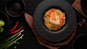 Vista superior de los fideos Schezwan o Chow Mein con verduras y pollo servidos en un plato negro sobre una mesa negra