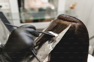 Produto saudável. Cabeleireira profissional usando luvas de proteção ao colorir o cabelo de sua cliente, usando instrumento estéril