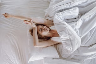 Top view of happy awaken young adult woman, spending good morning in cozy bedroom, lying in bed, stretch and smiling wide, resting at home on weekend