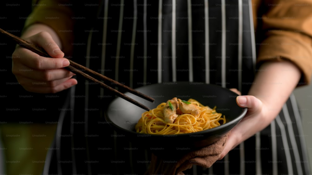 Close up view of a woman holding Schezwan Noodles or Chow Mein bowl and chopsticks