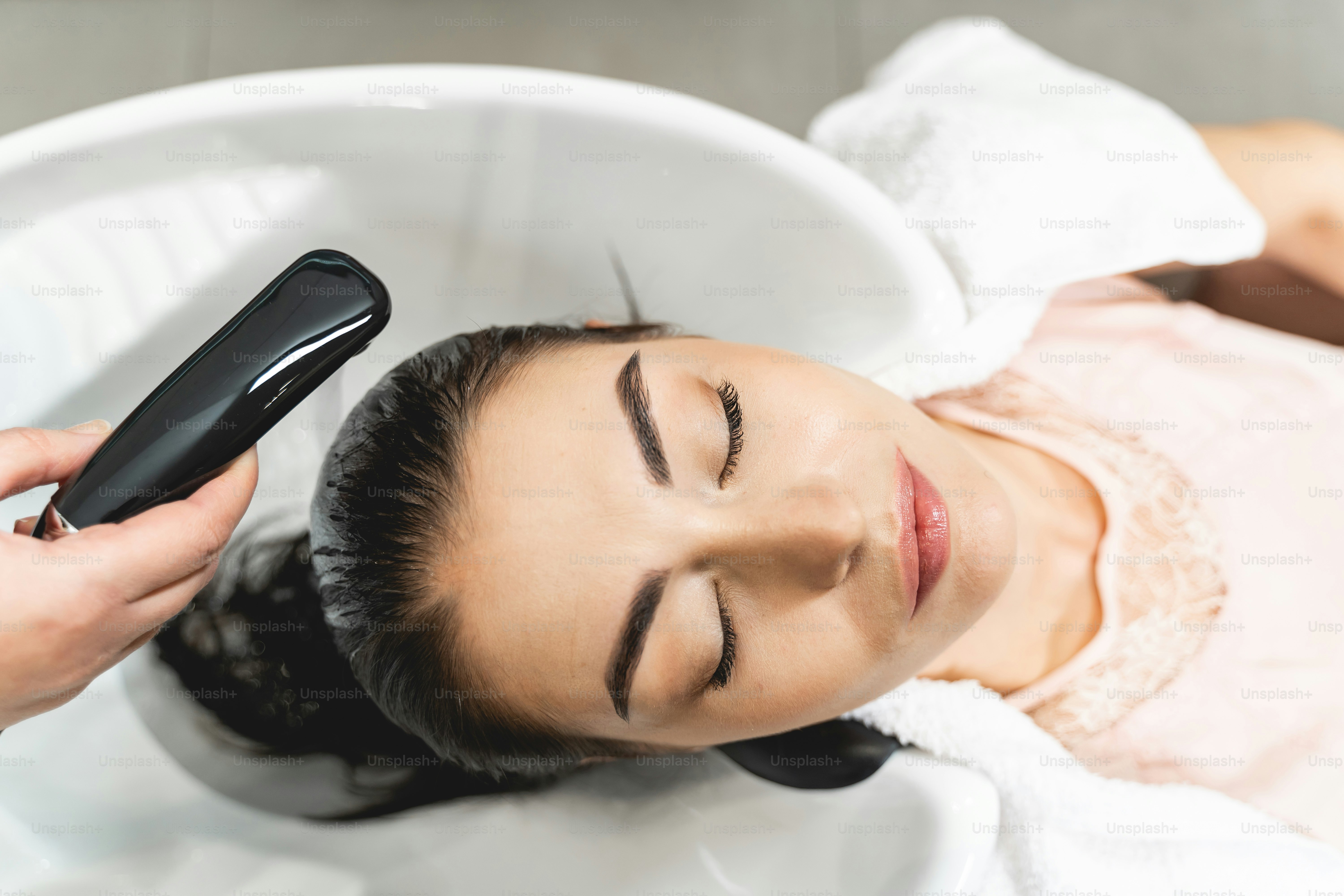 Schönheitsbehandlung. Freundliches brünettes Mädchen, das die Augen geschlossen hält, während sie ihre Haare vor dem Schneiden waschen lässt