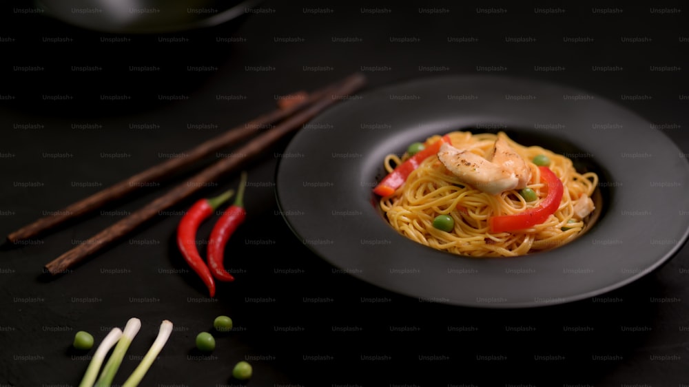 Cropped shot of Schezwan Noodles or Chow Mein with vegetable and chicken in black plate on black table