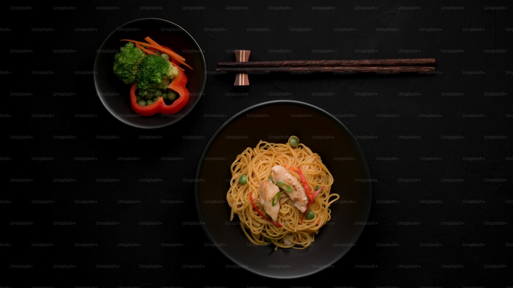 Draufsicht auf Schezwan Nudeln oder Chow Mein mit Gemüse, Hühnchen und Chilisauce serviert in schwarzer Schüssel