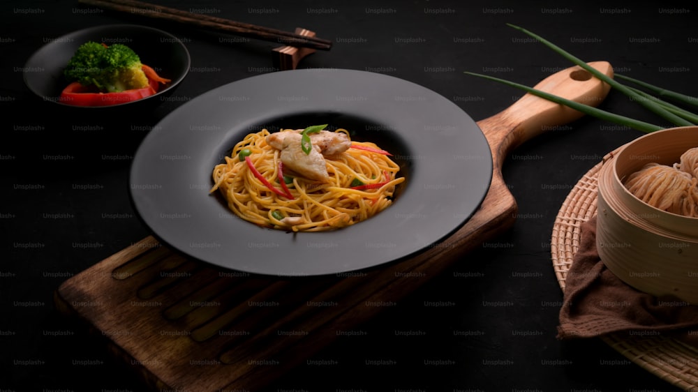 Cropped Shot von Schezwan Nudeln oder Chow Mein mit Gemüse, Hühnchen und Chilisauce serviert in schwarzer Platte auf Holzschreibtisch im chinesischen Restaurant