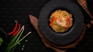 Draufsicht auf Schezwan Nudeln oder Chow Mein mit Gemüse und Hühnchen in schwarzem Teller auf schwarzem Tisch