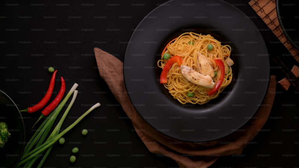 Top view of Schezwan Noodles or Chow Mein with vegetable and chicken in black plate on black table