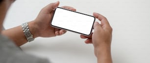 Cropped shot of male entrepreneur holding horizontal mock-up smartphone while sitting at simple working space