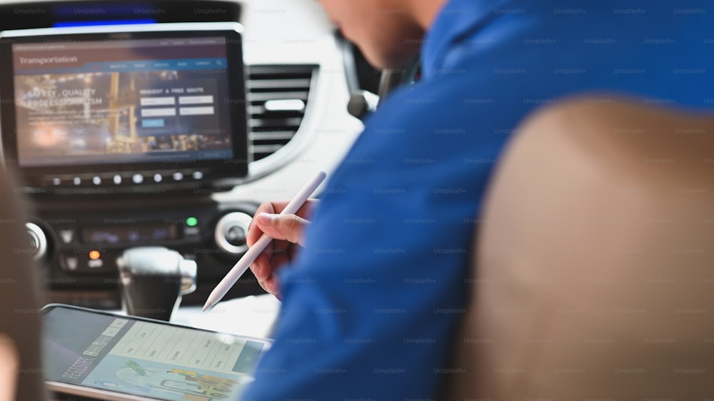 Imagen recortada del repartidor usando un lápiz óptico y una tableta de computadora para verificar la dirección de la ubicación del paquete mientras está sentado detrás del volante en la camioneta moderna.