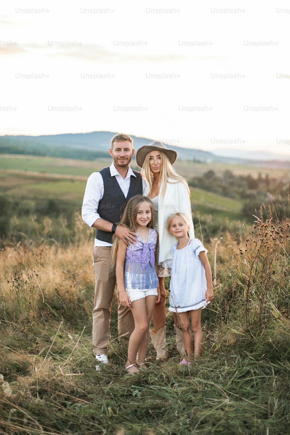 Portrait of happy family with children wearing stylish cowboy boho clothes standing in country field and looking at camera. Summer sunset in the field, family concept.