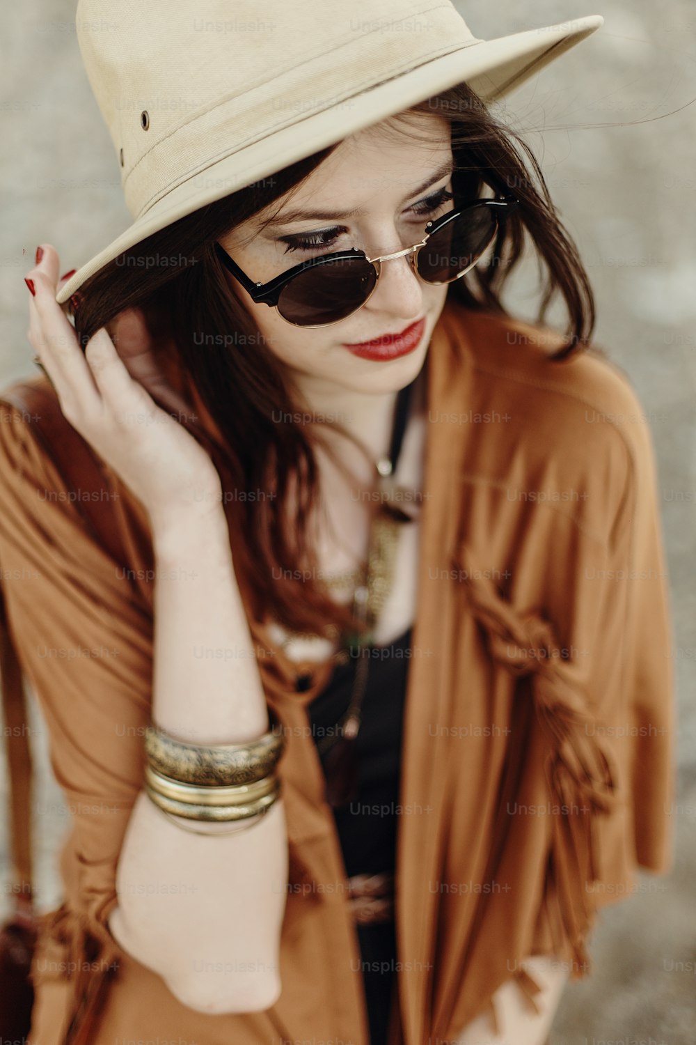 선글라스와 모자, 프린지 판초와 가죽 가방을 입은 아름다운 세련된 보헤미안 여자. 집시의 힙스터 소녀는 산의 강 해변 근처에서 포즈를 취하는 젊은 여행자를 봅니다. 관능적 인 표정.