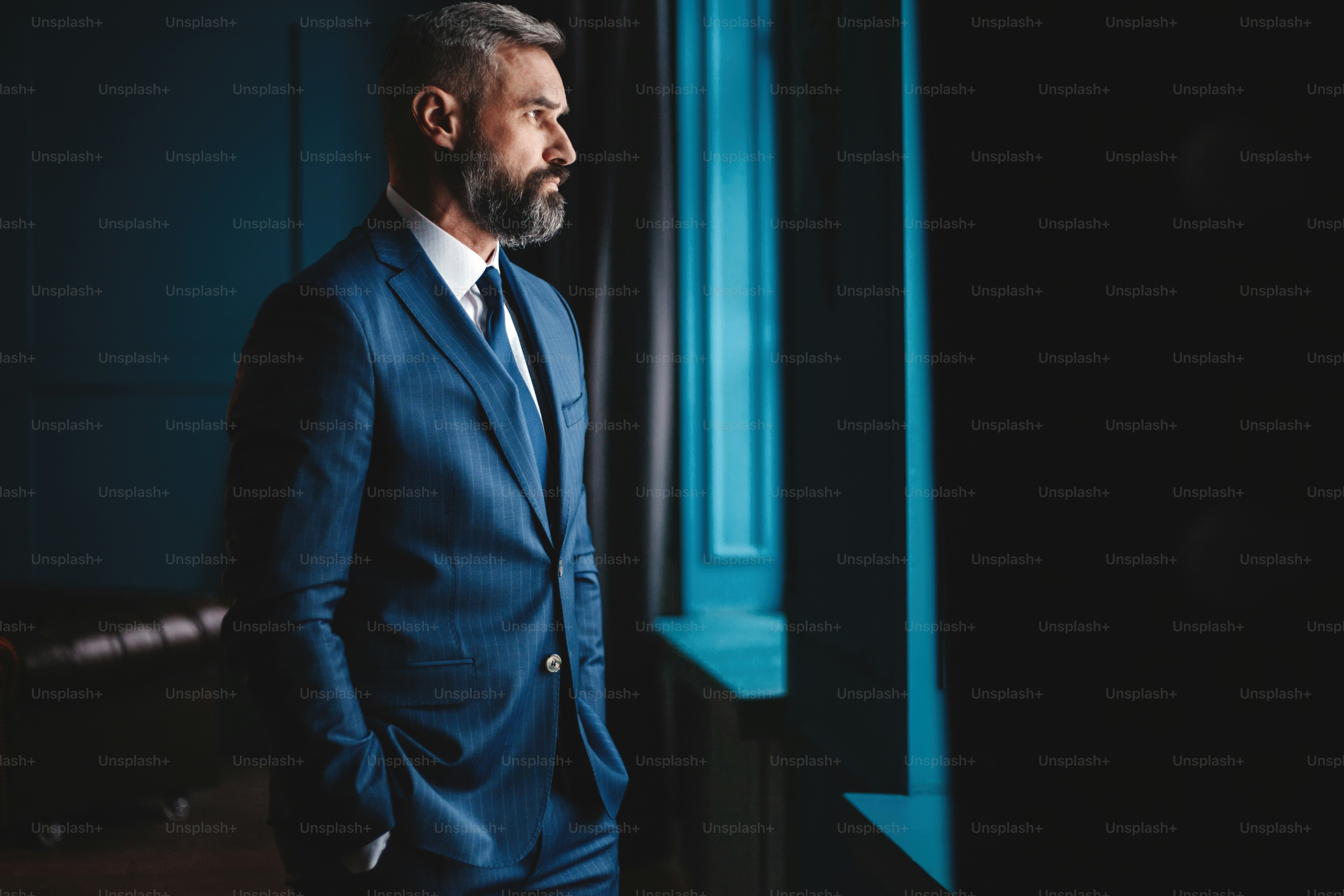 Thinking about... Thoughtful man in full suit looking away through the window while standing indoors